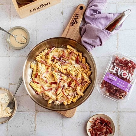 Pasta cremosa al gorgonzola con Fiammiferi di Speck Levoni servita all’interno di una padella da condividere, con crema avvolgente e bastoncini di speck in primo piano.