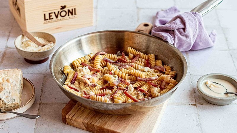 Pasta cremosa al gorgonzola con Fiammiferi di Speck Levoni servita all’interno di una padella da condividere, con crema avvolgente e bastoncini di speck in primo piano.