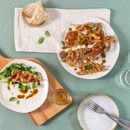 Scaloppine al vino bianco con Pancetta Levoni dorate e morbide, servite su piatti bianchi da portata accompagnate da foglioline di salvia e guarnite con la salsa al vino bianco ristretta.  