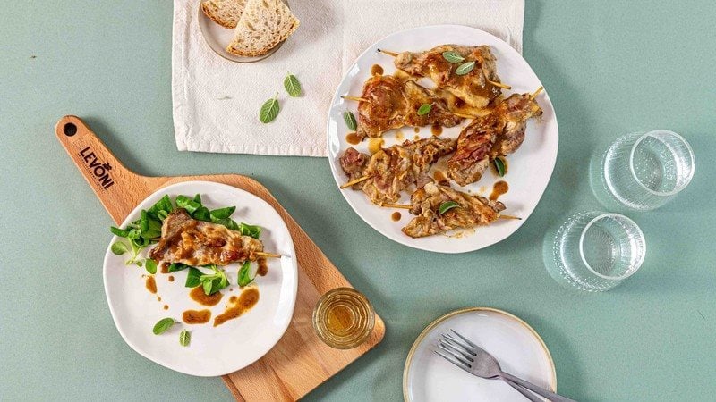 Scaloppine al vino bianco con Pancetta Levoni dorate e morbide, servite su piatti bianchi da portata accompagnate da foglioline di salvia e guarnite con la salsa al vino bianco ristretta.  