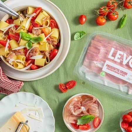 pasta fredda con Prosciutto Crudo Levoni, pomodorini ciliegino freschi e foglie di basilico verde, servita in una ciotola bianca prima di essere servita a tavola. 