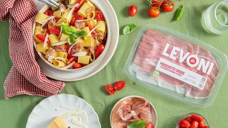 pasta fredda con Prosciutto Crudo Levoni, pomodorini ciliegino freschi e foglie di basilico verde, servita in una ciotola bianca prima di essere servita a tavola. 