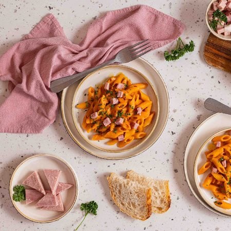 Piatto di penne al baffo cremose con dadini di Prosciutto cotto Alta Qualità Levoni, avvolte in salsa di pomodoro e panna vellutata, servite in un piatto con prezzemolo fresco tritato e una consistenza lucida.