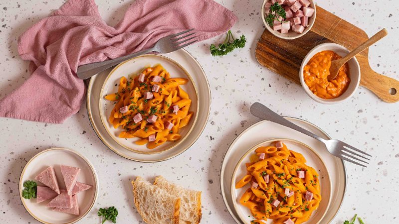 Piatto di penne al baffo cremose con dadini di Prosciutto cotto Alta Qualità Levoni, avvolte in salsa di pomodoro e panna vellutata, servite in un piatto con prezzemolo fresco tritato e una consistenza lucida.
