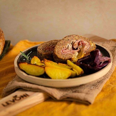 polpettone ripieno al forno con Prosciutto Cotto Alta Qualità Levoni e formaggio filante, tagliato a fette spesse, con crosta dorata e sughetto lucido, servito su piatto rustico con erbe fresche e fondo di cottura.