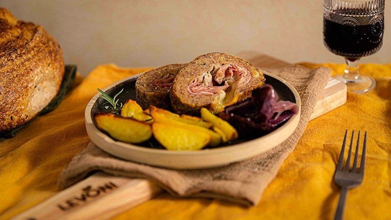 polpettone ripieno al forno con Prosciutto Cotto Alta Qualità Levoni e formaggio filante, tagliato a fette spesse, con crosta dorata e sughetto lucido, servito su piatto rustico con erbe fresche e fondo di cottura.