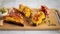 uova strapazzate cremose con Speck Levoni, Pancetta Levoni e Bacon Levoni, servite sopra una fetta di pane tostato, luce naturale e atmosfera da brunch artigianale.